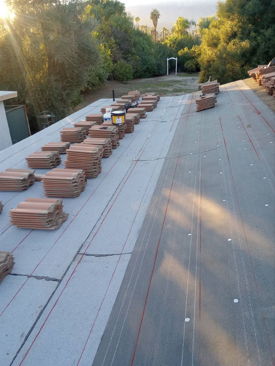 Tile re-roof in progress at golden hour, fresh tile stacked on new underlayment